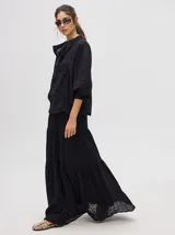 Camisa de broderie de algodón color negro, con cuello mao y cierre de cuatro botones. Presenta mangas abullonadas y galones con transparencias en la parte delantera y mangas.