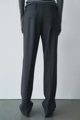 Pantalón de vestir gris oscuro de tiro bajo, con trabillas en la cintura, bolsillos delanteros y traseros, raya planchada y pierna recta.