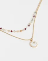Collar corto dorado de doble cadena, una de eslabones y otra con cuentas facetadas de colores. Incluye dije redondo esmaltado con detalle de strass.