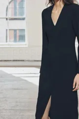 Vestido midi negro de escote pico y manga larga con hombreras. Tiene falsos bolsillos de vivo en el delantero y cierre en la espalda con cremallera oculta.