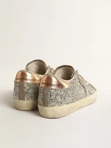Zapatillas deportivas estilo urbano con upper completamente cubierto de glitter plateado. Presentan detalles en gamuza color arena, incluyendo la estrella lateral característica. El talón tiene un acabado metálico color cobre. La suela es de goma color beige con efecto desgastado.