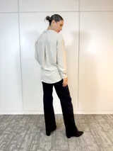 Camisa beige de poliéster con cuello clásico, cierre con botones y mangas largas con puños abotonados. Presenta detalles de brillos en cuello y puños.