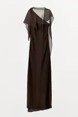 Vestido largo marrón con escote asimétrico y tirante ancho. Tiene una capa de tejido transparente a tono sobre el hombro y abertura lateral en el ruedo.