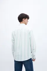 Camisa celeste con rayas verticales blancas, de corte regular, con cuello solapa clásico, bolsillo en el pecho y botones personalizados.