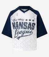 Remera de encaje blanco con mangas cortas raglán azul marino, cuello en V y estampado frontal con la inscripción "Kansas League Est. 1995".