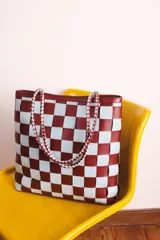 Bolso tipo tote de cuero trenzado a mano, con diseño a cuadros en color bordó y blanco.