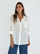 Camisa blanca traslúcida con cuello con detalle de encaje, manga larga y bolsillo en el pecho.