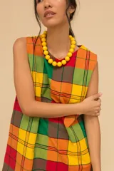 Vestido corto sin mangas con estampado de cuadros en tonos azul, rojo, verde y blanco. Tiene cuello redondo y ruedo con flecos.