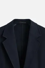 Blazer azul marino de corte recto, con cuello de solapa de muesca, cierre frontal con dos botones, bolsillos de solapa en la cadera y aberturas en la espalda. Confeccionado en tejido de algodón con elasticidad y sin forro interior.