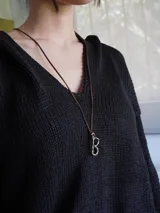 Gargantilla marrón de cuero con dije de bronce en forma de letra M.