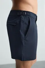 Short de baño celeste de tejido técnico con cintura elástica ajustable con cordón interior y trabillas laterales. Tiene bolsillos frontales y bolsillo trasero con cierre de cremallera. Cuenta con forro interior y cierre frontal con cremallera y botón a presión oculto.