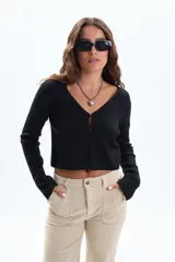 Saco de tejido punto negro con hilo de Lurex, escote en V y cierre frontal con botones. Presenta aberturas en los puños de las mangas largas.