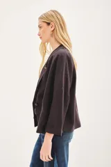 Saco de lino color negro, de corte amplio, con solapa, bolsillos falsos y pin de guitarra en la solapa.