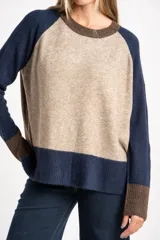Sweater de tejido de punto con diseño color block. Cuerpo principal en beige jaspeado, mangas y puños en azul marino, y detalles en marrón en el cuello y puños.