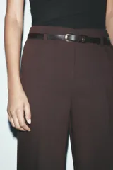 Pantalón marrón de tiro alto con cinturón negro, bolsillos delanteros y cierre frontal con cremallera y gancho metálico.