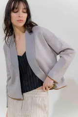 Chaqueta de punto color crudo con solapa ancha acanalada terminada con cadenetas en contraste negro. Tiene calce relajado, hombros caídos, largo a la cadera y manga larga.