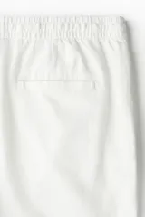 Pantalón de lino blanco, corte relaxed fit, con cintura elástica ajustable con cordón, bolsillos laterales y traseros.