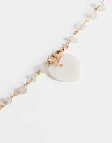 Collar largo con cadena dorada, detalles de piedras blancas irregulares y dije de corazón de nácar.