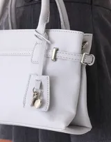 Cartera tipo city de cuerina color negro con correa con charm decorativo, manijas superiores con abrojo y cierre superior.