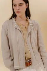 Saco tejido color beige con detalle de volados en el escote y la abertura frontal.