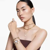 Reloj de pulsera con caja redonda dorada y brazalete metálico dorado adornado con cristales. La esfera es blanca con el logo del cisne a las 12 y tres cristales cuadrados como marcadores de índice. Es sumergible hasta 50 m.