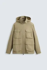 Parka color beige de tejido técnico ligero, corte relaxed fit, cuello alto con capucha plegable, manga larga con puños ajustables con botón a presión, cierre frontal con cremallera, cintura ajustable con elástico interno y múltiples bolsillos frontales de parche con solapa.