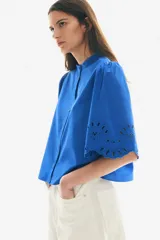 Blusa azul eléctrico de algodón con cuello mao, botones frontales, manga 3/4 abullonada con bordado calado y puños festoneados.