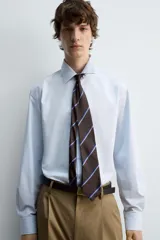 Camisa celeste de algodón con estructura twill, corte regular, cuello solapa, manga larga con puños abotonados y cierre frontal con botones.