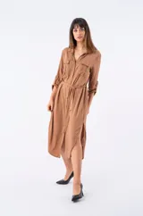 Vestido camisero midi color marrón, con cuello camisero, cierre frontal con botones, mangas largas con trabillas y bolsillos con solapa en el pecho. Incluye cinturón de la misma tela.