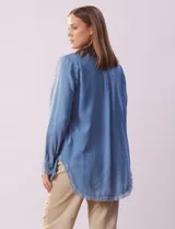Camisa celeste de tencel marca Hester & Orchand, con cuello con solapa, escote en V y abertura central con botones. Tiene un bolsillo aplicado en la delantera y ruedo desflecado.