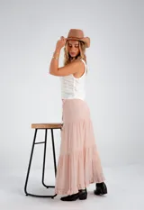 Pollera larga de color rosa pálido, con corte en capas y cintura elastizada. Incluye lazo fino del mismo material.