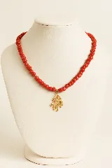 Collar corto de cuentas redondas de nácar color rojo, con dije colgante dorado en forma de rama de coral.