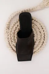 Sandalia marrón de cuero con punta cuadrada, talón abierto y faja ancha. Tiene detalle de elástico oculto en la cara interna de la capellada. El forro y la plantilla son de cuero vacuno.