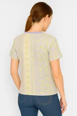 Remera amarilla con estampado de motivos playeros en blanco: soles, olas y conchas marinas.