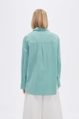 Camisa a rayas verticales verdes y blancas, de corte holgado, manga larga con puños abotonados, cuello clásico y bolsillo de parche en el pecho.