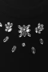 Camiseta negra de manga corta y cuello redondo con apliques de strass y cuentas plateadas alrededor del cuello.