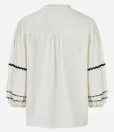 Blusa color crema de tricolina con detalles de ondas negras en cuello, mangas y frente. Tiene mangas 3/4 con volados y lazo en el cuello.