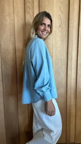 Blusa blanca con textura de lunares, cuello con volados, cierre parcial con botones y mangas largas con puños abotonados.