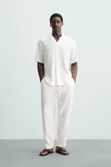 Camisa de calce relajado confeccionada en tejido fluido de mezcla de viscosa, color blanco. Presenta cuello bowling, manga corta, aberturas laterales en el bajo y cierre frontal con botones al tono.