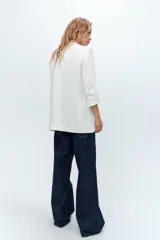 Blazer blanco con cuello solapa y hombreras. Manga por debajo del codo acabada en vuelta con trabilla y botón dorado. Bolsillos delanteros con solapa.