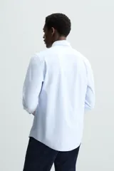 Camisa celeste a rayas verticales blancas, de corte recto, con cuello italiano abierto, mangas largas con puños abotonados y cierre frontal con botones.