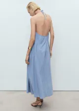 Vestido largo de mezclilla, color azul claro, con escote de pico y tirantes finos ajustables. Presenta un detalle de lazo en el centro del escote y un corte recto que se ensancha ligeramente hacia el ruedo.