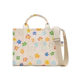 Bolso tote mediano de lona color crema con estampado de margaritas de colores. Tiene cierre superior con cremallera, asas superiores de lona resistente y correa de cincha ajustable y extraíble.