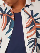 Camisa blanca de manga corta con estampado de hojas en negro y gris, cuello clásico y corte recto.