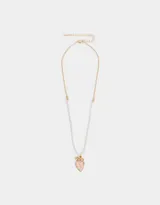 Collar corto con cadena dorada y perlas sintéticas. Dije de corazón esmaltado en rosa con borde dorado y detalle de moño dorado en la parte superior.