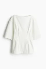 Remera larga color blanco de punto pesado de algodón, con escote barco, hombros caídos, mangas al codo y cintura entallada con pinzas acolchadas.