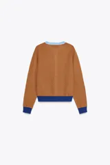 Chaqueta marrón de punto con cuello redondo y manga larga. Presenta cierre frontal con botones y detalles color block en azul en cuello, puños y ruedo.