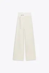Pantalón de tiro alto color crema, de corte palazzo, con cinturón ancho de tela con hebilla metálica.