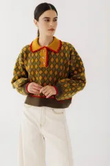 Sweater de punto con diseño de rombos en tonos ocre y verde oliva. Tiene cuello polo amarillo con borde rojo, cierre parcial con botones y puños acanalados con borde rojo.