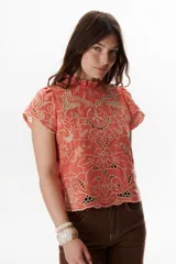 Blusa color coral o terracota con bordado calado floral en tono beige claro. Presenta cuello alto con volado y mangas cortas abullonadas.